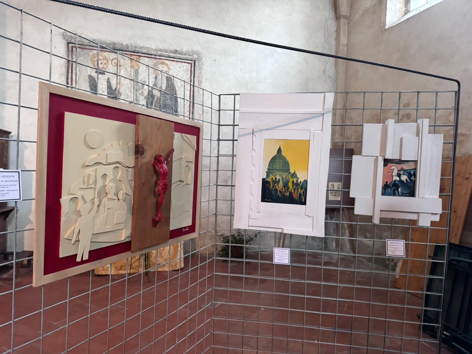 Dettaglio ravvicinato di opere esposte su pannelli reticolari in chiesa